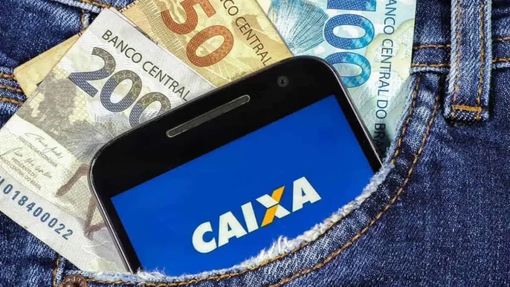 Notas de R$ 200, R$ 50 e R$ 100, junto a um celular que mostra o logo da Caixa Econômica Federal, no bolso de uma calça jeans